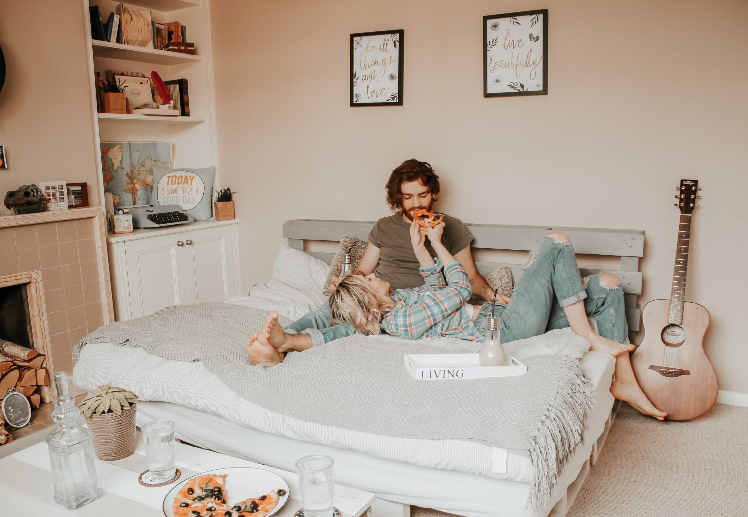 Woman feeds man pizza as they cuddle on the bed